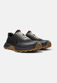 Scarpe da ginnastica nere con una combinazione di mesh testurizzato e gomma liscia, con lacci crema e una suola in gomma color caramello con un motivo di trazione.