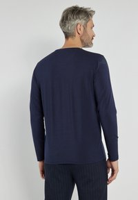 Granatowa koszula z długim rękawem, wykonana z miękkiego materiału, z okrągłym dekoltem, minimalnym przeszyciem i luźnym krojem. Widok z tyłu.