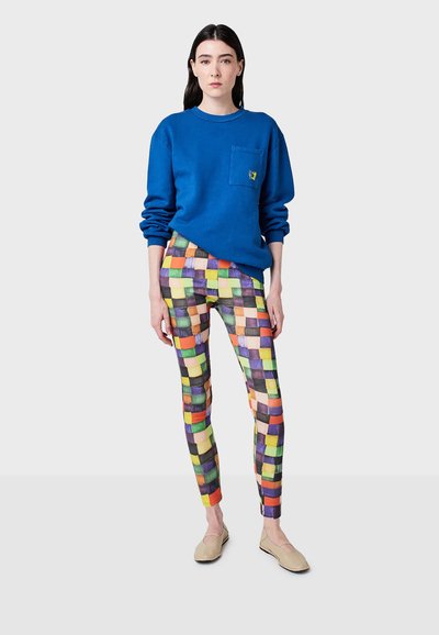 Felpa blu con tasca, leggings a scacchi colorati in varie tonalità e ballerine beige. Texture morbide e design casual.