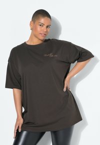 Hnědé oversized tričko s krátkým rukávem, na kterém je v světlejším odstínu napsáno "Nemanželské příběhy". Měkká látka a uvolněný střih.