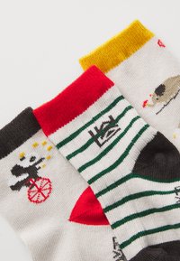 Calze per bambini in dimensioni ridotte con colori vivaci: strisce nere, rosse, verdi e gialle. I motivi includono un monociclo, animali fantasiosi e dettagli grafici.