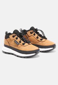Hnědé semišové a černé síťované turistické boty s bílou podrážkou, které mají černé tkaničky a kontrastní logo na boku.