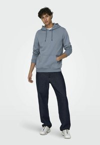 Lichtblauwe hoodie met een voorzak, cinched zoom en verstelbare trekkoorden. Gepaard met donkerblauwe jeans en witte sneakers.