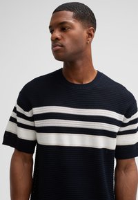 Marineblauer Strickpullover mit weißem Streifenmuster über der Brust und an den Ärmeln. Rundhalsausschnitt, kurze Ärmel und strukturiertes Material.