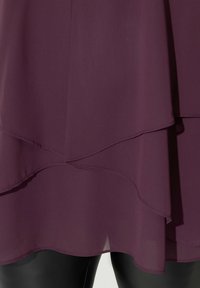 Abito bordeaux con orlo a strati, realizzato in tessuto leggero. Presenta una superficie liscia e un taglio ondulato ai bordi.