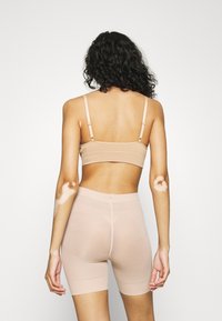 Nude sömlös bralette med justerbara axelremmar, i kombination med matchande mid-thigh shorts. Båda har en mjuk, stretchy tyg.