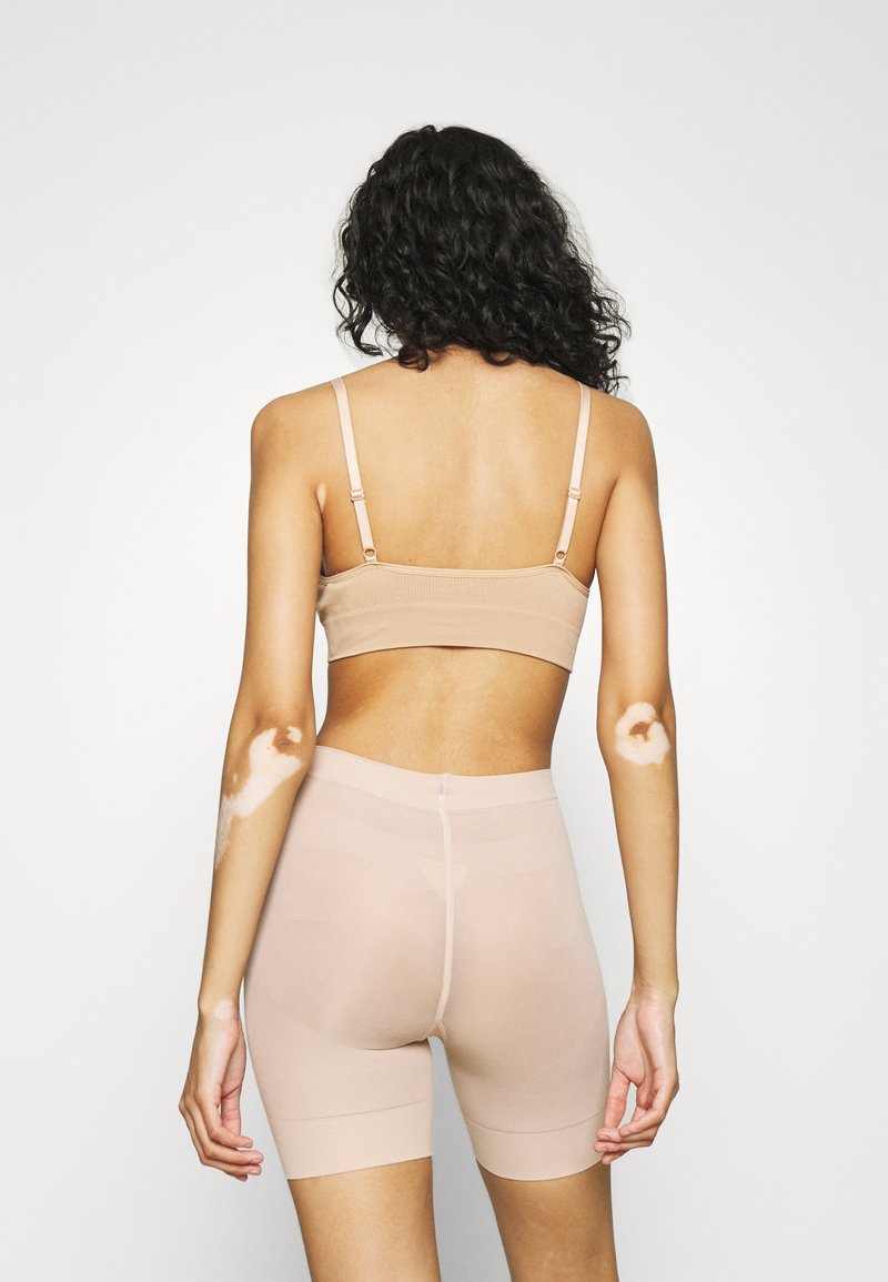 Nude sömlös bralette med justerbara axelremmar, i kombination med matchande mid-thigh shorts. Båda har en mjuk, stretchy tyg.