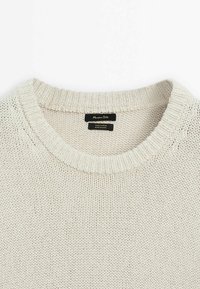 Maglione lavorato a maglia beige chiaro con scollatura rotonda, realizzato in 100% cotone. Presenta un orlo e dei polsini a costine, rivelando un motivo testurizzato.