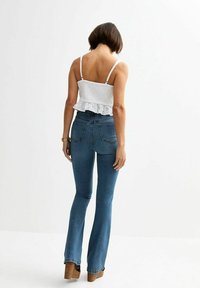 Vit ögla peplumtop med tunna axelremmar, kombinerad med högmidjade blå utsvängda jeans som har två bakfickor och en åtsittande silhuett.