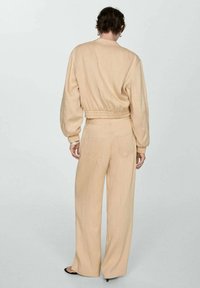 Beige cropped jack met elastische tailleband en brede mouwen, gecombineerd met bijpassende wijde broek. Lichtgewicht, gestructureerde stof.