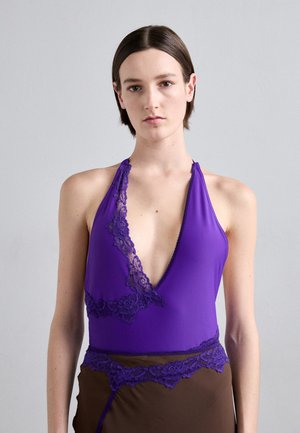 Top halter violet cu un decolteu adânc în V, evidențiat de o dantelă delicată neagră pe linia gulerului și pe margine, combinat cu o parte inferioară maro.
