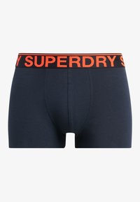 Boxers en bleu marine fabriqués en coton doux, dotés d'une taille élastique noire ornée d'un lettrage orange audacieux "SUPERDRY".