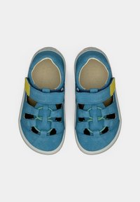 Μπλε παπούτσια από σουέντ με κλειστή μύτη, με ανοίγματα και κίτρινο λουράκι. Υφή στην επιφάνεια και αντιθετικές πράσινες λεπτομέρειες.