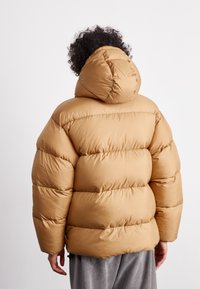 Puffjakke i lysbrun, quiltet design med hætte, med en blød, glat tekstur og en fyldig silhuet til varme.