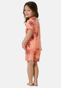 Komplet piżamy z krótkim rękawem w kolorze brzoskwiniowym, z jasnym, abstrakcyjnym wzorem słońca w brązowych i żółtych kolorach. Zawiera szorty z postrzępionymi brzegami.