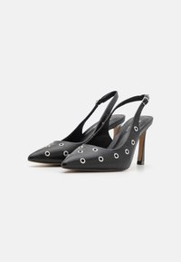 Tacchi slingback in pelle nera con punta affusolata, caratterizzati da dettagli in ottone argentato a forma di occhio circolare e un sottile tacco a stiletto.