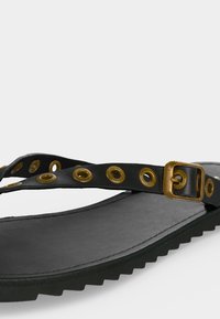 Μαύρο σανδάλι με υφή στην σόλα, λεπτό λουράκι με χρυσούς κρίκους και ρυθμιζόμενη χρυσή αγκράφα.