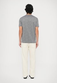 Szara koszulka z krótkim rękawem z logo rozmieszczonym na całej powierzchni, zestawiona z szerokimi spodniami w kolorze ecru. Prosty design, minimalistyczne akcenty, casualowy krój.