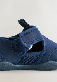 Námornícky modré slip-on topánky vyrobené z textílie s sieťovými panelmi, textúrovanou gumovou podrážkou a suchým zipsom pre bezpečné uchytenie.