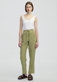 Lehké olivově zelené kalhoty s elastickým pasem a bočními kapsami, doplněné otištěným bílým topem na ramínka a tmavými sandály.