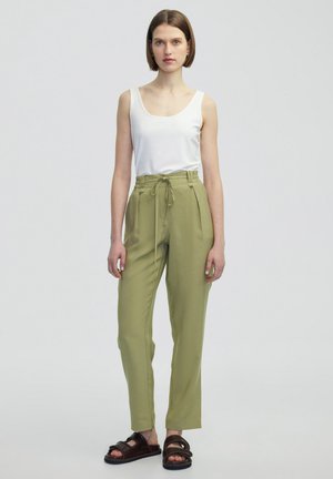 Pantalones livianos de color verde oliva con cintura ajustable y bolsillos laterales, combinados con una camiseta ajustada blanca y sandalias oscuras.