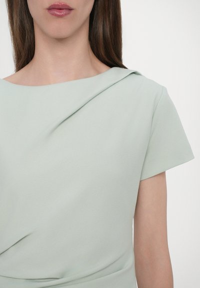 Rochie verde deschis cu decolteu tip barcă, mâneci scurte și un design plisat, având o textură netedă și moale.