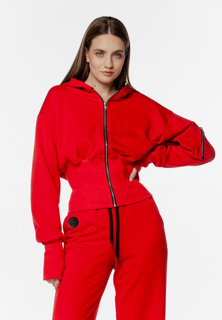 Czerwona bluza z kapturem na zamek, z wysokim kołnierzem, długimi rękawami i ściągaczami, w zestawie z pasującymi czerwonymi spodniami z czarnym akcentem.