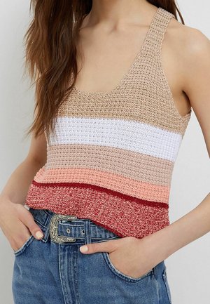 Donna che indossa un top all'uncinetto senza maniche multicolore con strisce orizzontali infilato in un paio di jeans blu con fibbia della cintura d'argento incisa.