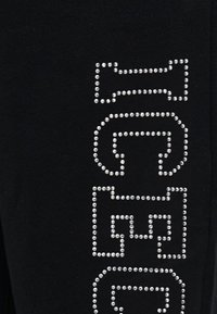 Τέσσερα κάθετα γεωμετρικά σχήματα από μικρές ασημένιες τρούκ σε μαύρο ύφασμα.