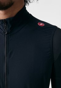 Gilet da ciclismo nero con colletto alto, zip frontale a metà, vestibilità slim e dettaglio logo rosso sulla spalla. Realizzato in materiale elasticizzato e traspirante.