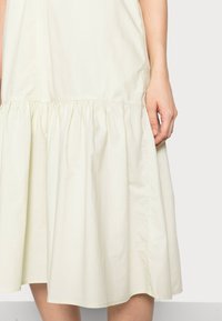 Helles gelbes, aus Baumwollmischung bestehendes Kleid mit gerafftem Taillenteil und ausgestelltem Rock, das eine glatte Textur und minimalistische Nähte aufweist.
