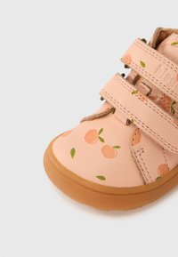 Ροζ δερμάτινο παπούτσι με σχέδια ροδάκινου, διαθέτει δύο λουριά με βέλκρο και λαστιχένια σόλα. Στρογγυλερή μύτη και ραφτά διακοσμητικά κατά μήκος των ακρών.