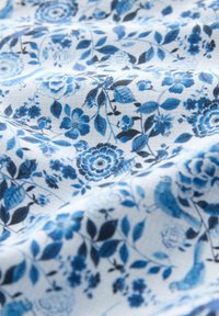 Bawełniana tkanina z niebieskim kwiatowym wzorem na białym tle, z różnymi kwiatami, liśćmi i drobnymi detalami ptaków.