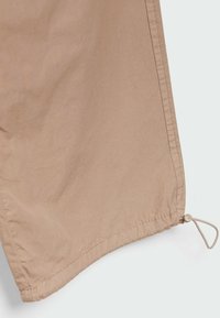 Tela beige con una textura suave que cuenta con un cordón con tope en el dobladillo. El diseño incluye una costura limpia a lo largo del borde.