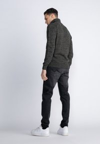 Maglione a collo alto lavorato a maglia grigio scuro con polsini a coste, indossato con pantaloni neri e sneakers bianche. Texture liscia con un motivo sottile.