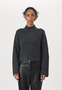 Maglione grigio scuro a coste con collo alto e design corto. Maniche lunghe e larghe in tessuto texture, abbinato a pantaloni in pelle neri.