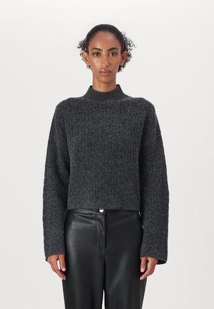 Dark gray, ribbed knit sweater with a high neck and cropped design. Long, wide sleeves and textured fabric, paired with black leather pants.