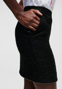 Black sequin skirt with textured surface and side pocket. Hem features a silver beaded trim. Form-fitting silhouette and high waistband.