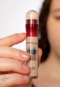 Correcteur Maybelline Instant Anti-Age dans un tube beige avec un capuchon rouge, doté d'un embout applicateur intégré et d'un dôme transparent.