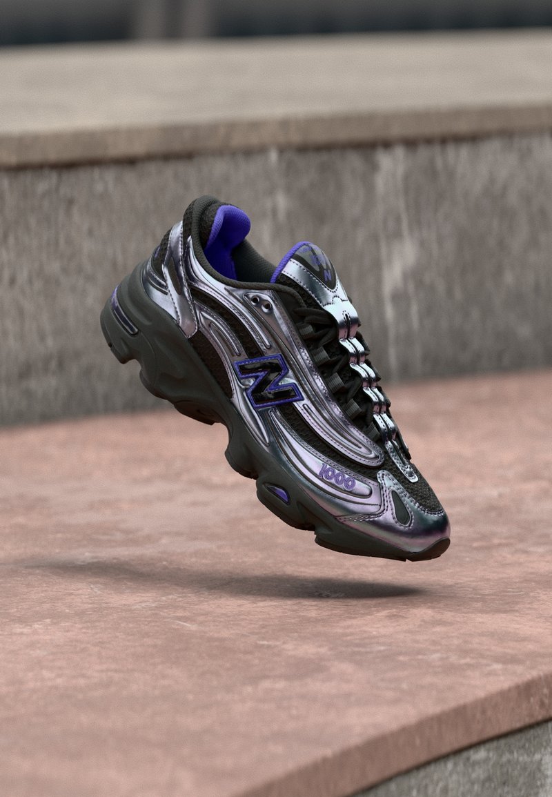 Baskets New Balance 1000 noires et violettes en plein vol au-dessus d'une surface en béton avec un mur de pierre flou en arrière-plan.