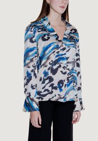 Seidenbluse mit einem abstrakten Muster in Blau, Schwarz und Creme, einem spitzen Kragen und langen Ärmeln mit breiten Manschetten. Knopfleiste vorne.