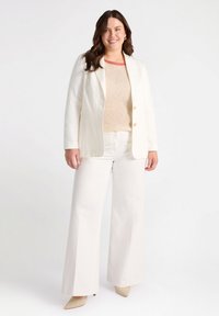 Kołnierzykowy żakiet w kolorze kości słoniowej z złotymi guzikami, w zestawieniu z beżowym swetrem i szerokimi spodniami w kolorze kości słoniowej. Model nosi beżowe szpilki.