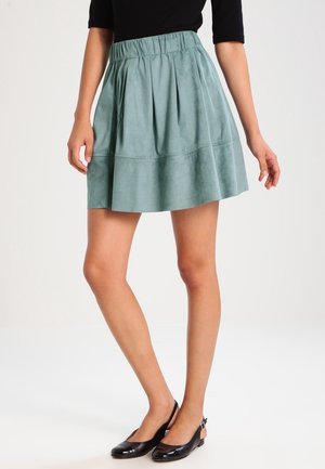 Une jupe plissée teal en feutre synthétique doux, présentant une taille élastique et un design évasé, atteignant le mi-thigh.