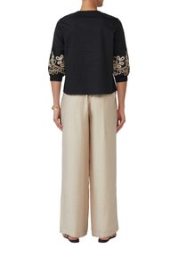 Zwart top met driekwart mouwen met gouden geborduurde bloemenpatronen. Gecombineerd met lichtbeige wijde broek, wat zorgt voor een contrasterende look.