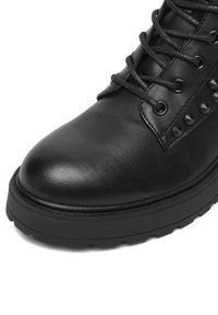 Czarne skórzane botki za kostkę z okrągłym noskiem, sznurowanym zapięciem i dekoracyjnymi czarnymi ćwiekami po bokach, z teksturowaną podeszwą.