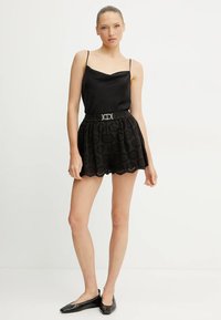 Camisola di raso nera con spalline sottili abbinata a pantaloni corti neri con motivi circolari ricamati e un orlo scallop, accentuati da una cintura.