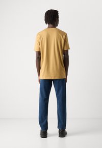 Short-sleeve yellow cotton T-shirt, relaxed fit, paired with blue denim pants and black footwear, viewed from the back.