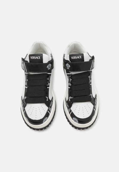 Svarta och vita sneakers med läder- och textilmaterial, framträdande snören, kardborrband och intrikata mönster på sidorna.