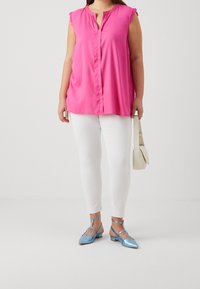 Fuchsiová bezrukávová blůza s krajkovým lemem, v kombinaci s bílými skinny kalhotami a modrými metalickými sandály na řemínky. Nese malou béžovou kabelku.