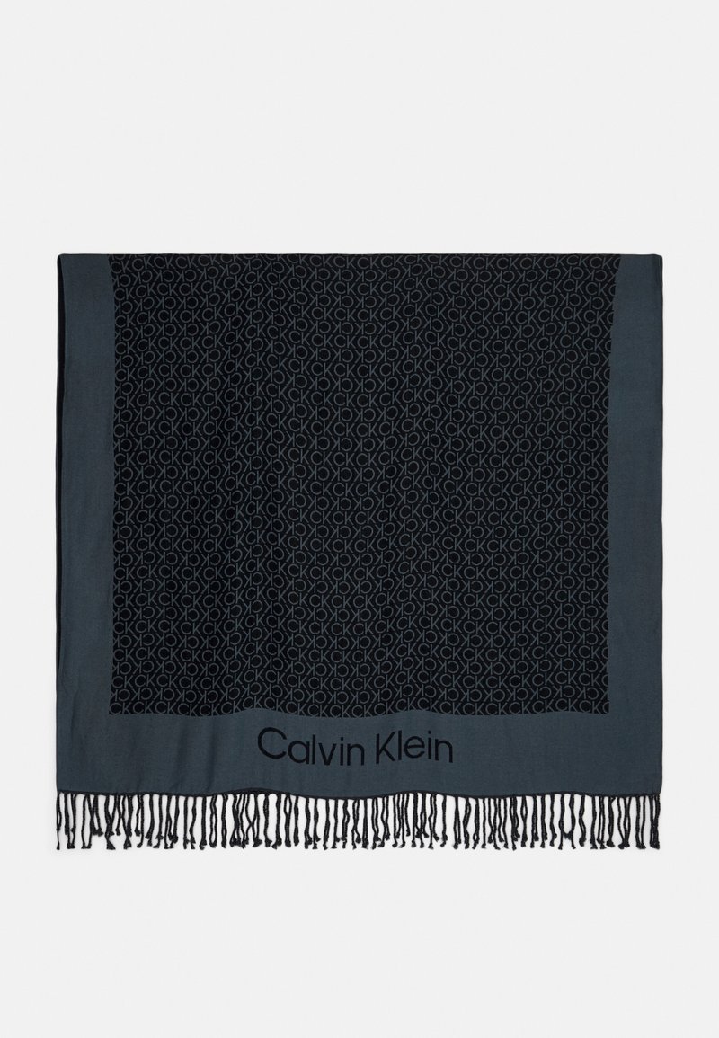 Écharpe rectangulaire noire et gris foncé avec motif répété "CK" et texte "Calvin Klein", finie avec une frange noire sur un bord.